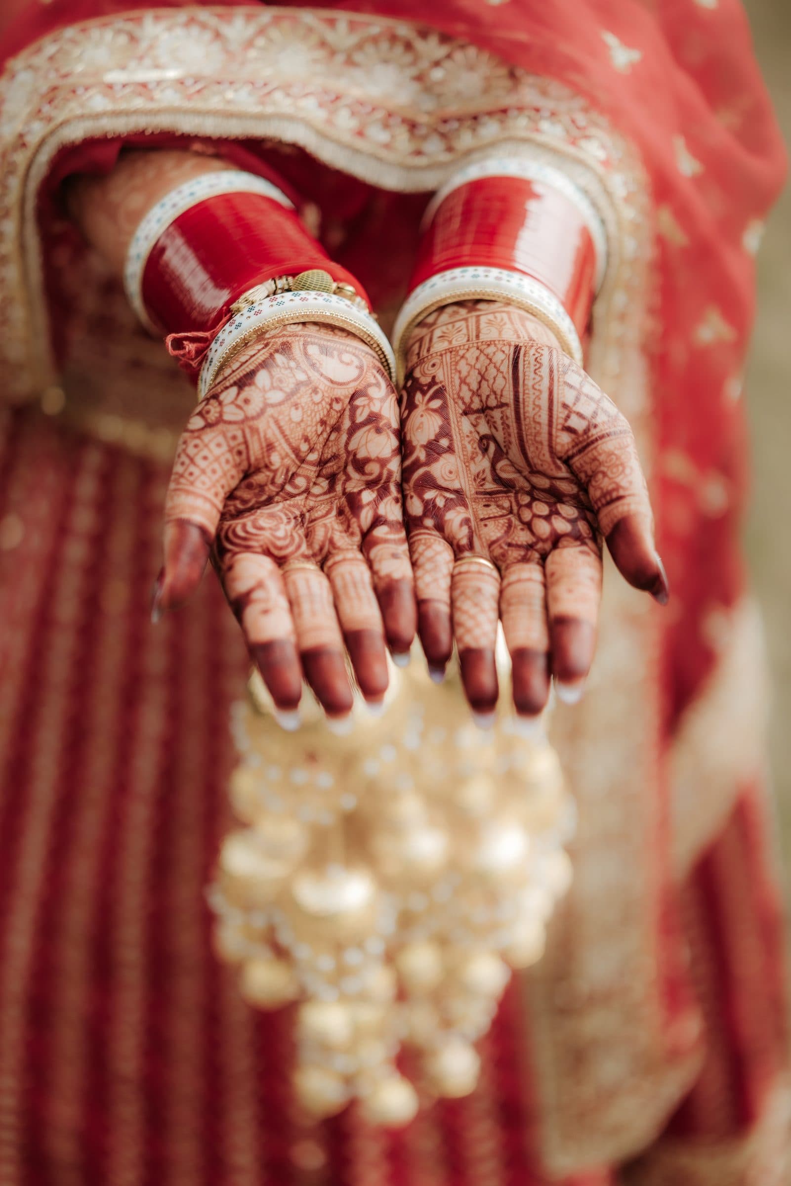 A close-up of a bride's henna-adorned hands and bridal jewelry